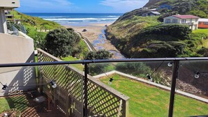 A coastal view from a balcony with a sea, beach, and houses in the background. - Comfort and the best seat in the west to view the Tasman Sea (Baylys Beach)