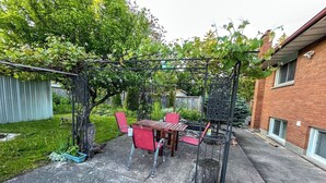 Une terrasse avec une table et des chaises, une pergola et, au fond, un bâtiment en briques.
