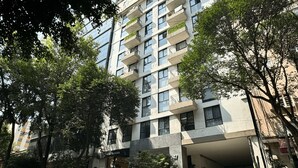 Un immeuble à plusieurs étages doté de balcons, une voiture garée devant et des arbres tout autour.