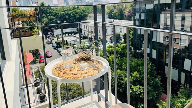 A balcony with a round table, potted plants, and a view of a cityscape with modern buildings. - Nice Apartment Perfect Location Ext View. (Ciudad de México)