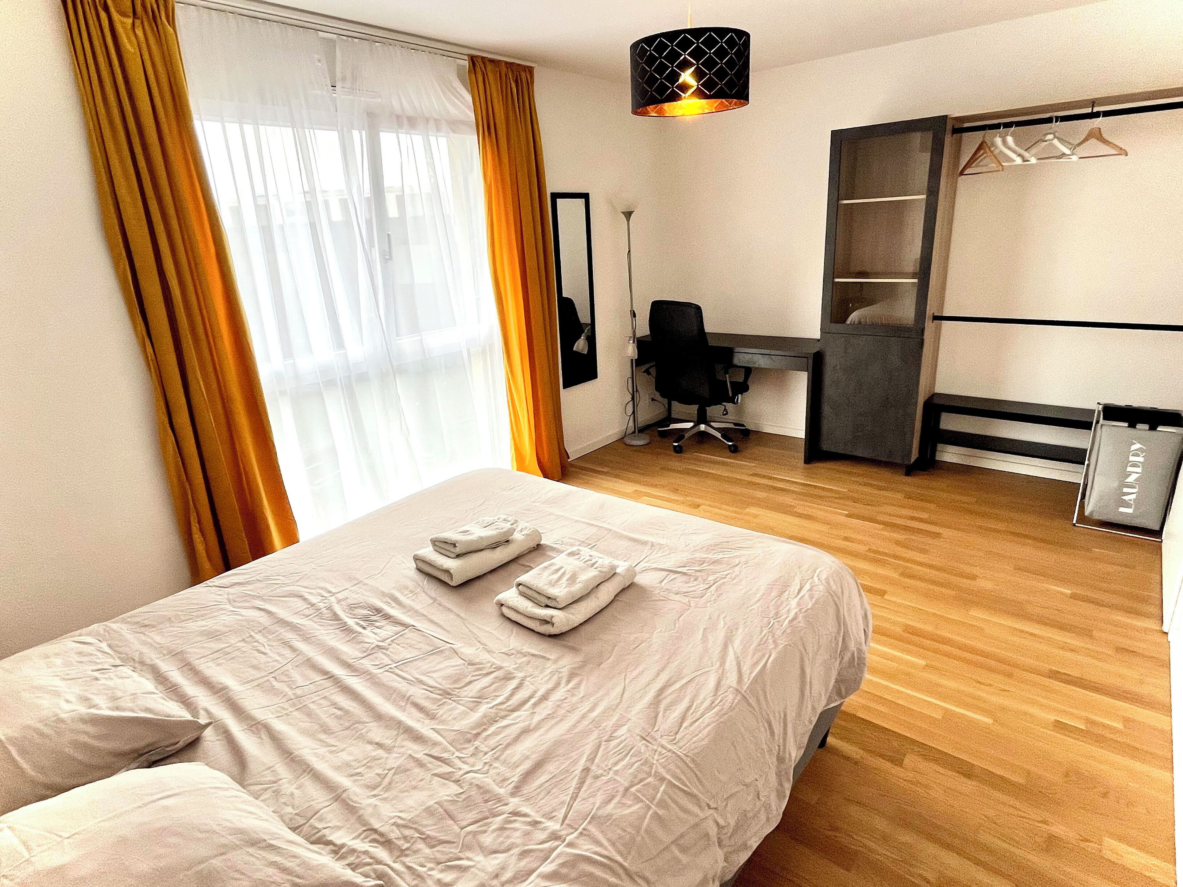 A hotel room with a bed, a desk, a chair, a wardrobe, and a hanging light fixture.