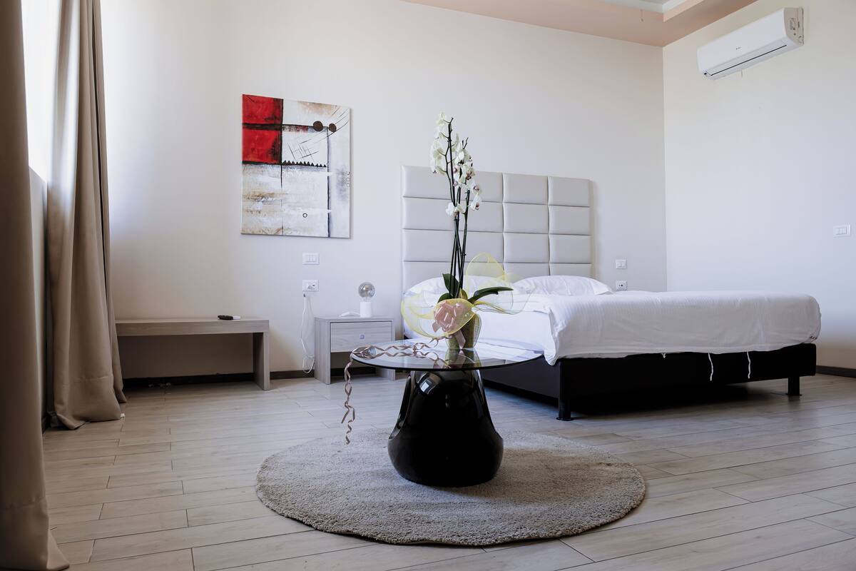 Ein modernes Schlafzimmer mit einem Bett, einem Nachttisch und einer dekorativen Vase mit Blumen.