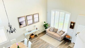 A spacious living room with a beige sofa, a dining table with chairs, and a chandelier. - Spacious Poolside Oasis - Right Next to Beach and Legoland (Vista)