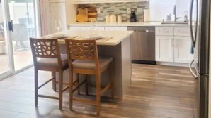 A modern kitchen with wooden flooring, a central island with bar stools, white cabinets, and pendant lighting. - Spacious Poolside Oasis - Right Next to Beach and Legoland (Vista)