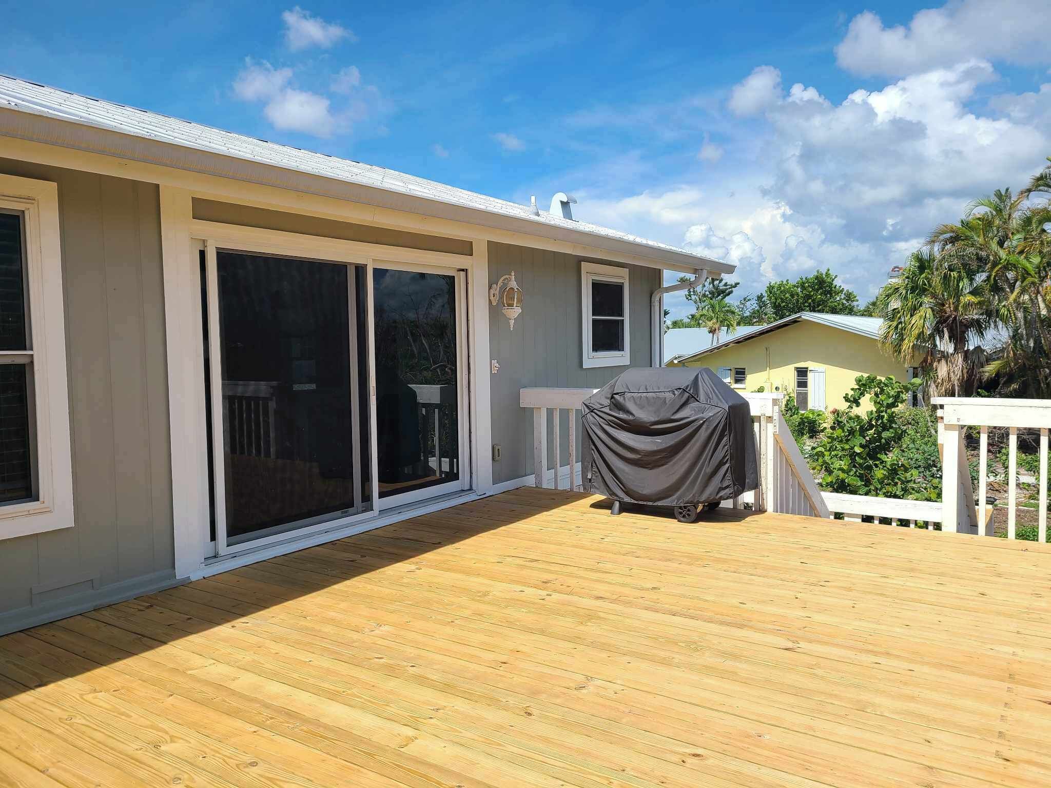Een overdekt terras met een barbecue, een schuifpui en een witte balustrade.