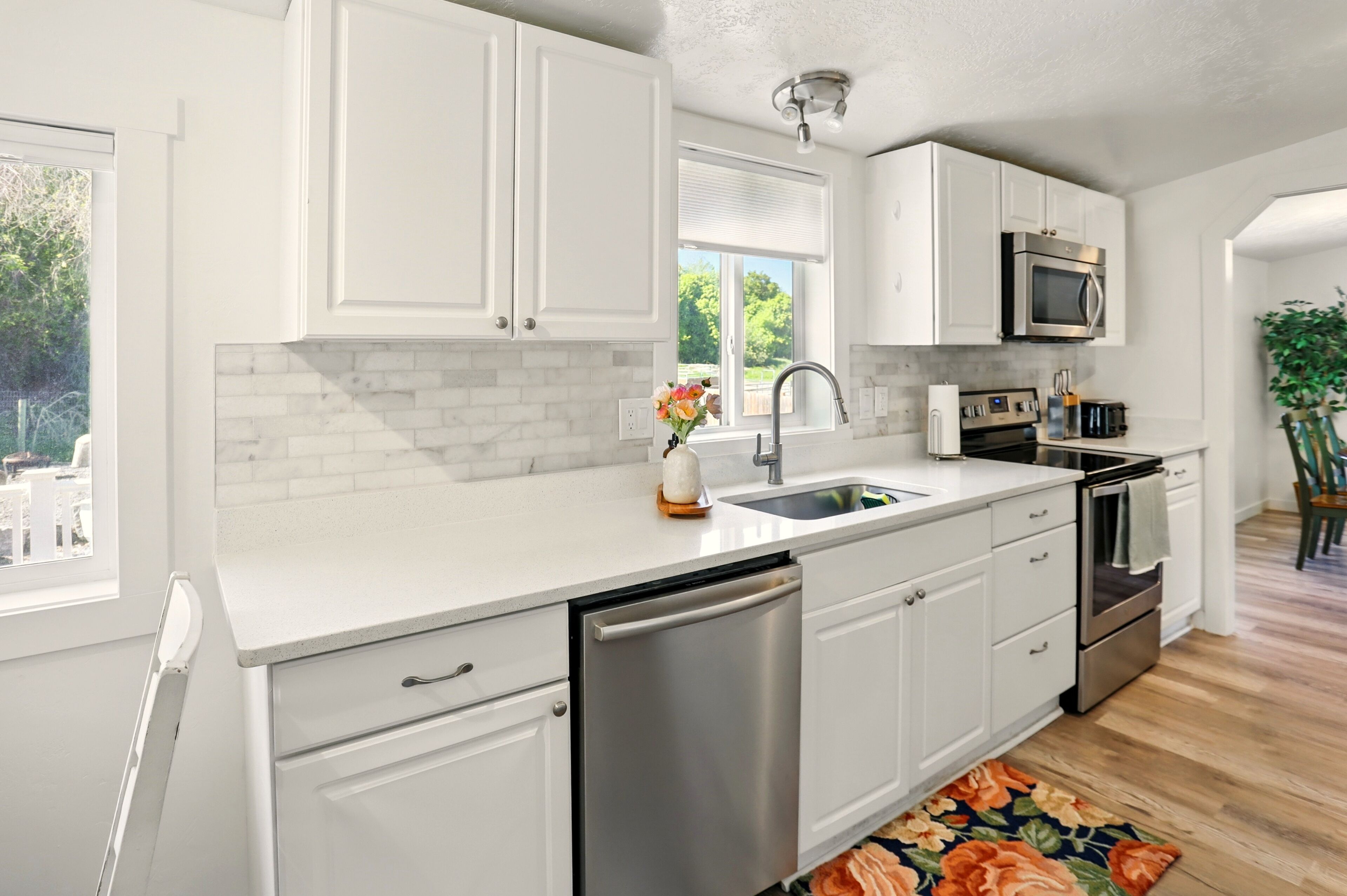 Una cocina moderna con muebles blancos, lavavajillas de acero inoxidable, horno integrado y microondas.