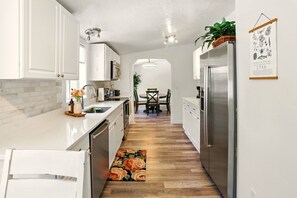 Una cocina moderna con armarios blancos, un refrigerador de acero inoxidable, piso de madera y un comedor con mesa y sillas.