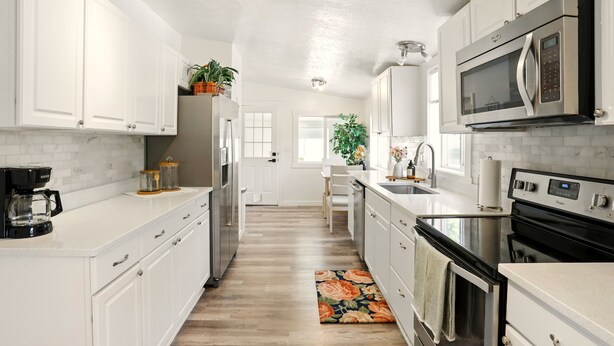 A modern kitchen with white cabinets, stainless steel appliances, and a wooden floor.