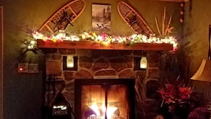 Una chimenea de piedra con repisa de madera decorada con luces y flores, un cuadro enmarcado encima, y una etiqueta que dice "Lake Kawaguchiga".