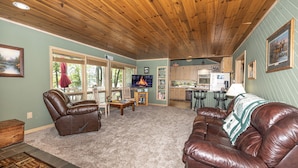 Amplia sala de estar con sofás de cuero, techo de madera y vista a la cocina.