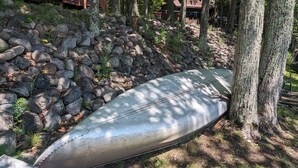 Una terraza de madera con un muro de piedra y una canoa apoyada contra árboles.