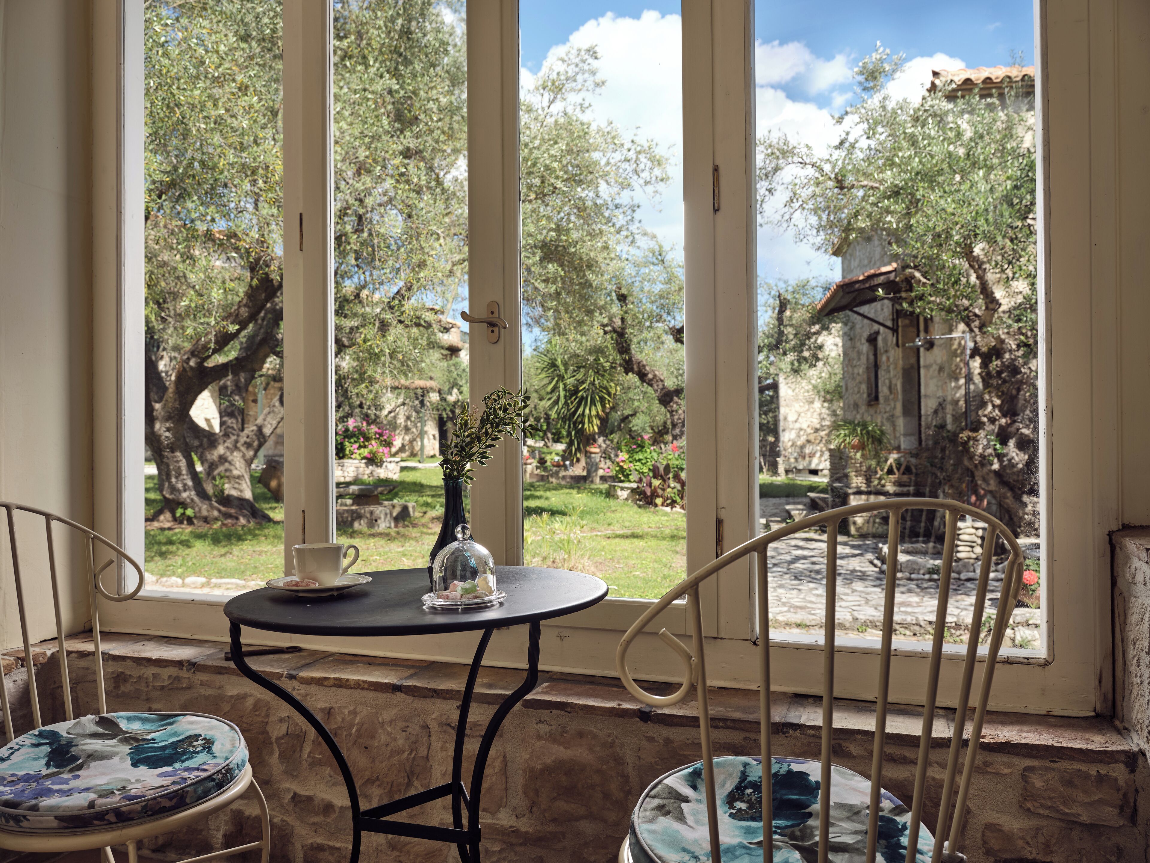 Une pièce donnant sur un jardin grâce à de grandes fenêtres, avec une petite table ronde et deux chaises aux motifs colorés.