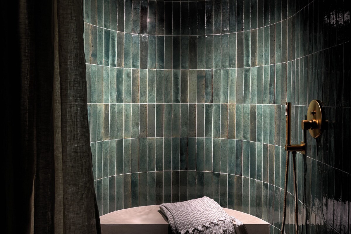A modern bathroom with a curved shower area, a bathtub, and a towel rack.