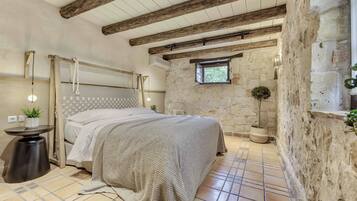 Un dormitorio con pared de piedra, techo de madera, cama con manta tejida, una ventana pequeña y una planta en maceta.