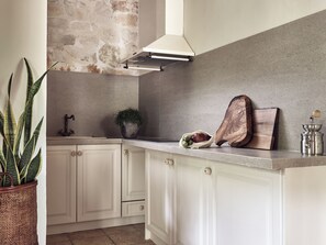 A kitchen with white cabinets, a stone wall, a hanging light fixture, a potted plant, and a coffee grinder. - Leeda's Villas (Zakynthos)