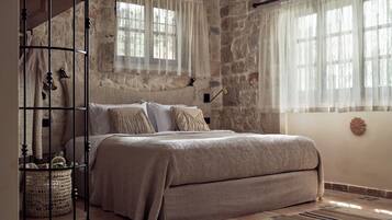 A bedroom with a stone wall, a bed with a beige blanket, a wicker basket, and a wooden headboard.