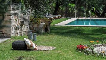 Un área de piscina con un muro de piedra, sillas de descanso y césped.