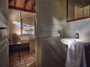Une salle de bain avec un lavabo blanc, un miroir et une serviette accrochée au mur. On y trouve une étagère avec des articles de toilette et une petite table sur laquelle est posée une bougie.