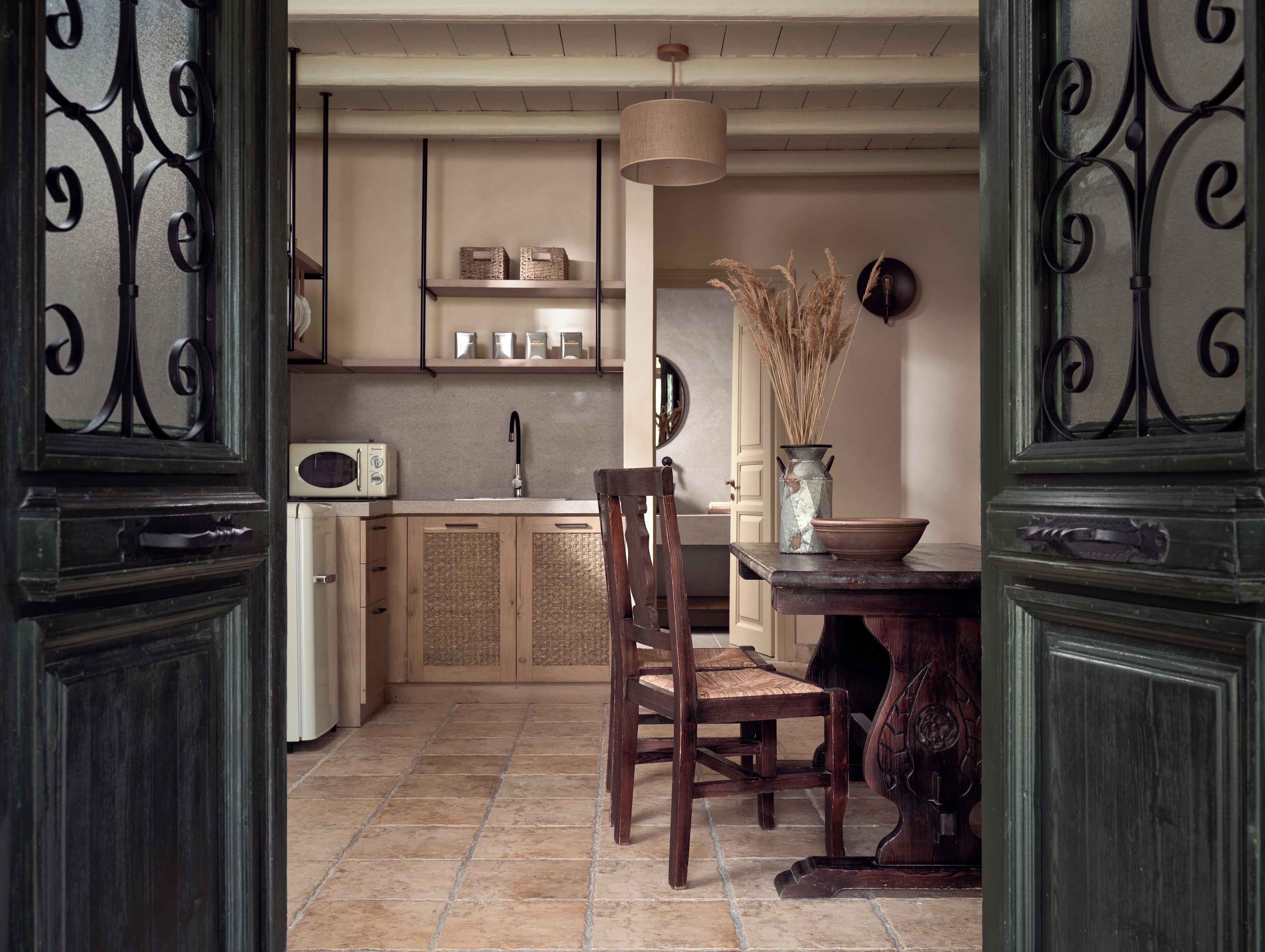 A kitchen with a wooden table, chairs, a microwave, and a vase with dried plants.