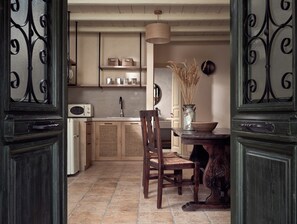 A kitchen with a wooden table, chairs, a microwave, and a vase with dried plants. - Leeda's Villas (Zakynthos)