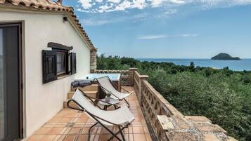A terrace with a table and chairs, a view of the sea, and a distant island.