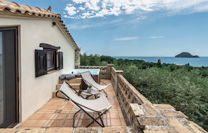 Une terrasse avec une table et des chaises, une vue sur la mer et une île lointaine.