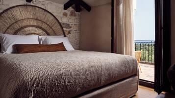 A bedroom with a stone wall, a large bed with a woven headboard, and a balcony with a view.