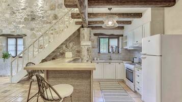 A kitchen with a central island, white cabinets, a stainless steel refrigerator, and a stone wall.