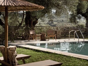 Un área de piscina al aire libre con sillas de madera, una baranda de metal y una sombrilla de paja.