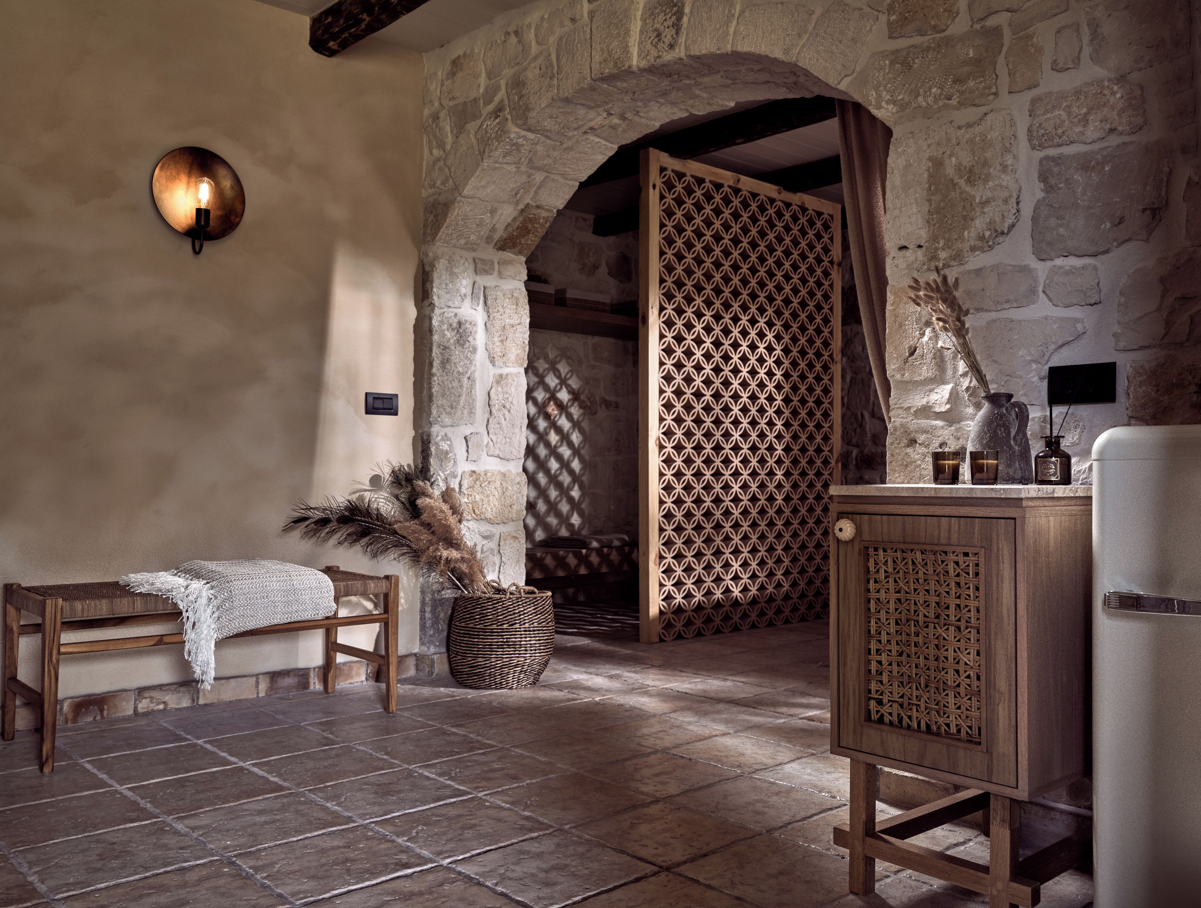A rustic interior with stone walls, a wooden bench, a woven basket, and a cabinet.