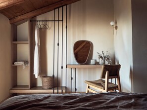 Un dormitorio con cama, una silla de madera, una estantería con espejo y un perchero.