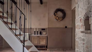 Una escalera con barandillas negras, una pared con una cesta tejida y velas, y una pared de piedra con un nicho decorativo.