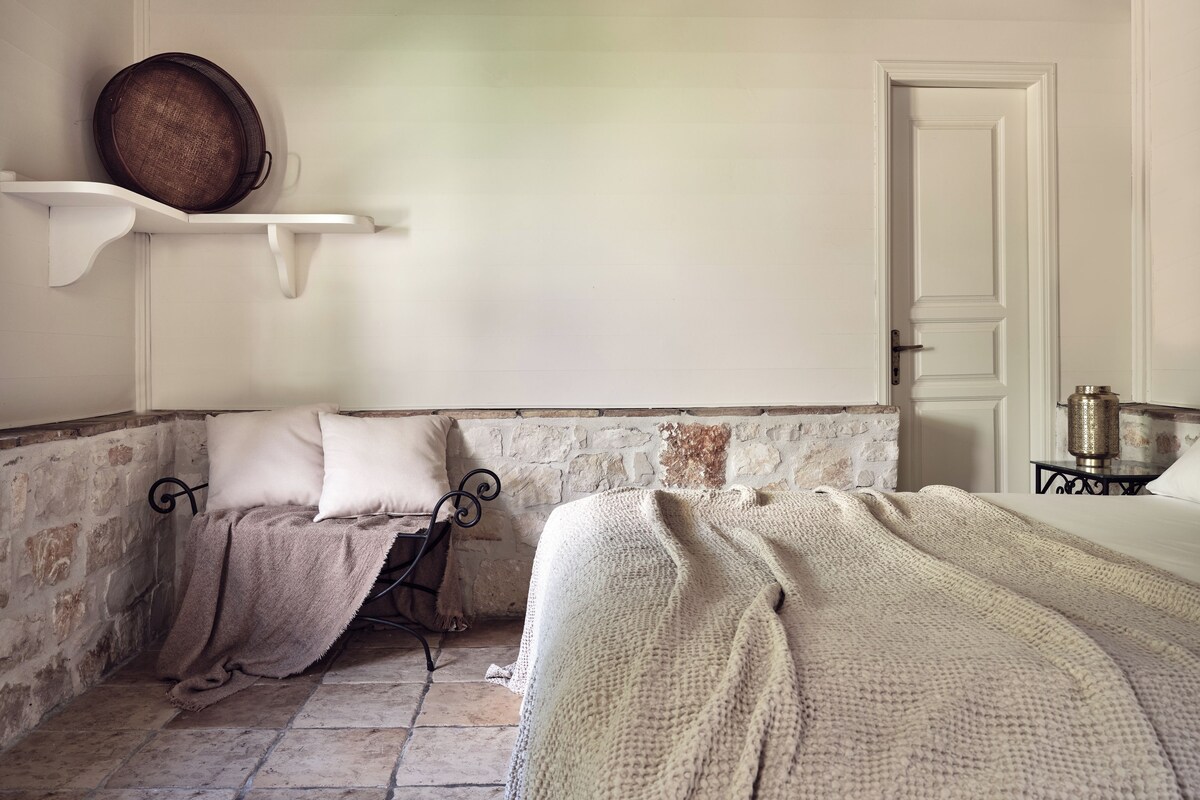 Una habitación con dos camas, una pared de piedra, una puerta blanca y un estante con una cesta.
