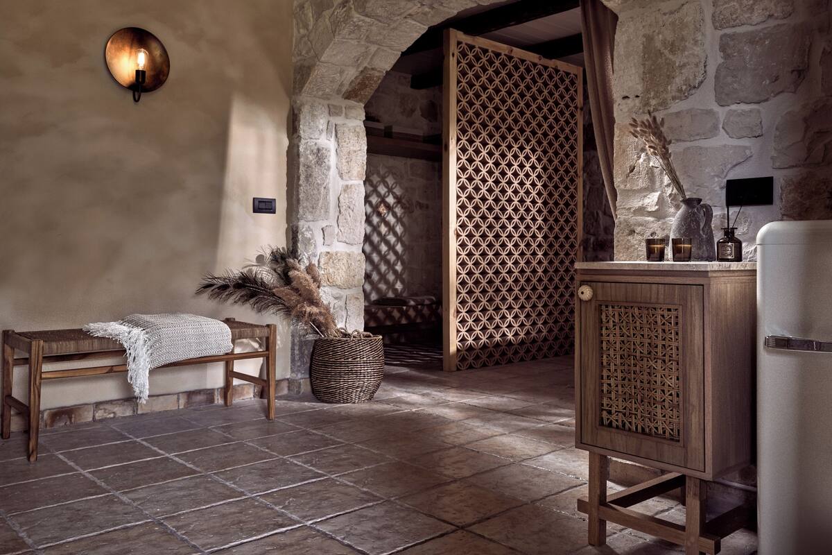 A rustic room with stone walls, a wooden bench, a woven basket, and a cabinet with a decorative screen.