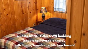 Una stanza in legno con un letto, una lampada e una finestra. Testo che invita gli ospiti a portare la propria biancheria da letto.