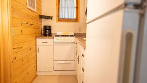 Una cucina compatta con pareti in legno, un fornello, una moka e un frigorifero.