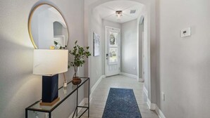 A hallway with a mirror, a lamp, a plant, and a blue rug.