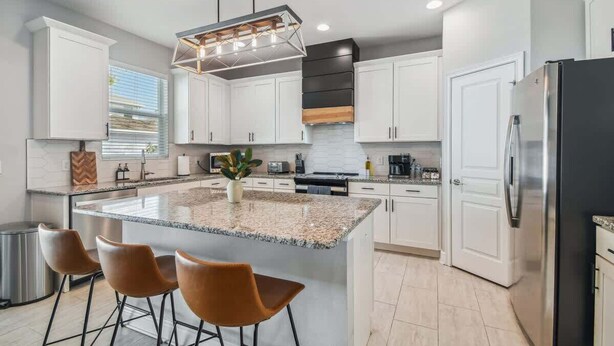 A modern kitchen with white cabinets, a granite island, stainless steel appliances, and a pendant light.