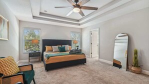 A bedroom with a bed, a ceiling fan, a window, a nightstand, a chair, and a mirror.