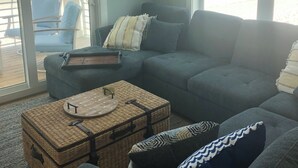 A living room with a grey sofa, a wicker coffee table, and a view of the beach through large windows. - Closest to the sand and surf and no better view than Water’s Edge in the sand  (Port St. Joe)