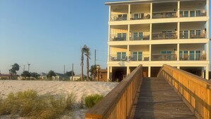 A wooden boardwalk leading to a multi-story building with balconies, situated on a sandy beach with sparse vegetation. - Closest to the sand and surf and no better view than Water’s Edge in the sand  (Port St. Joe)