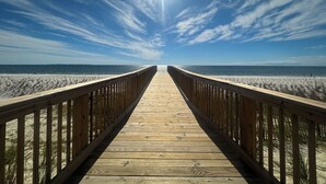 A wooden boardwalk leading to a beach with a clear sky. - Closest to the sand and surf and no better view than Water’s Edge in the sand  (Port St. Joe)