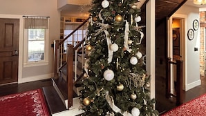 Un vaste espace de vie agrémenté d’un grand sapin de Noël, d’un escalier en bois et d’un chien allongé sur un tapis rouge.