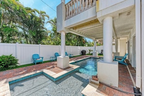 A swimming pool with a brick deck and blue chairs, surrounded by a white fence and palm trees. - Island Nautilus managed by Beach Retreats FL pool, 2 min walk to beach, elevator AMI (Bradenton Beach)