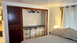 Un dormitorio con cama, armario de madera, escritorio pequeño y mesita de noche.