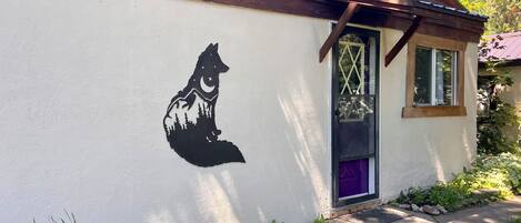 A house with a mural of a wolf on the side, a purple door, and a small window.
