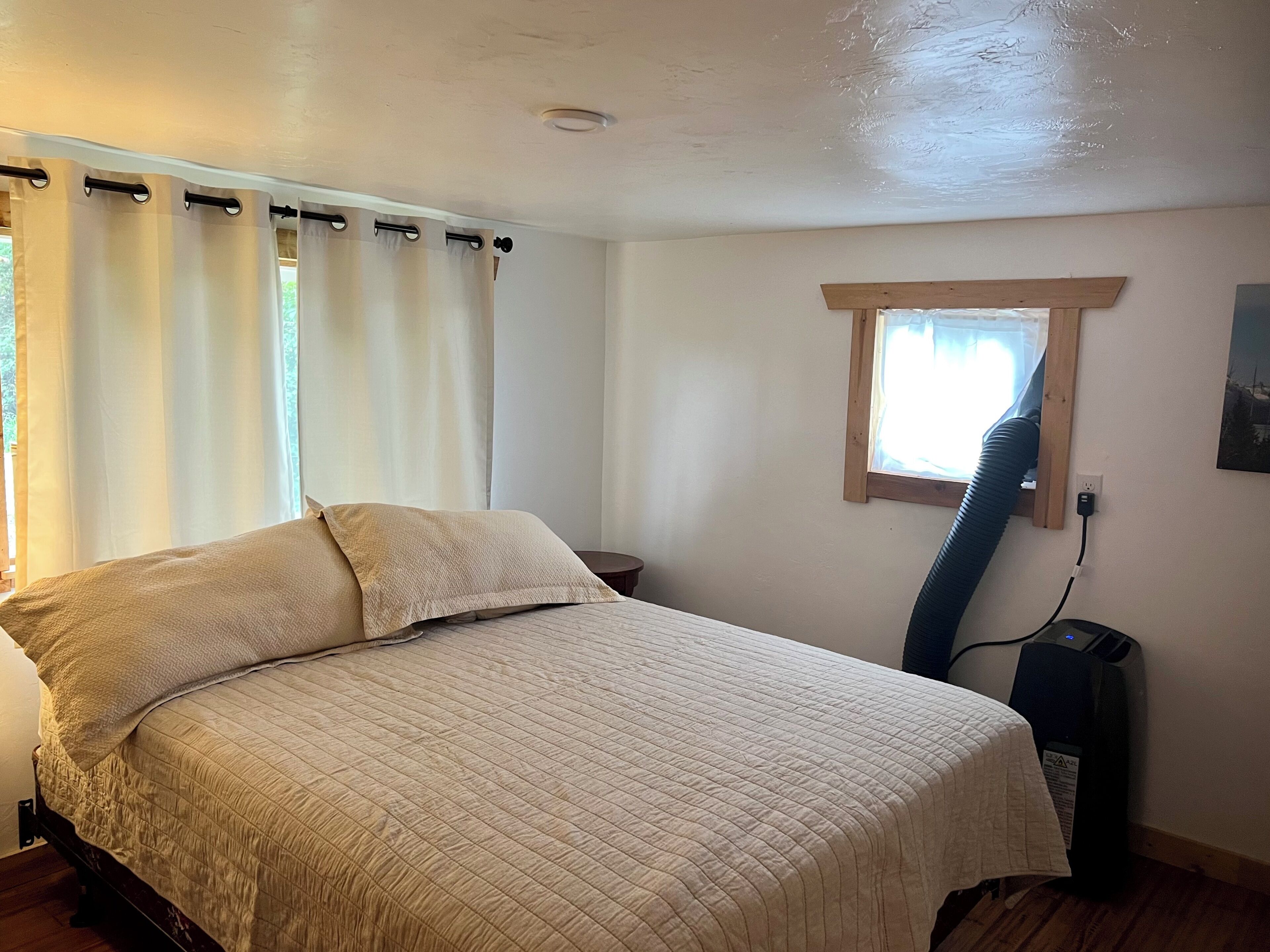 A bedroom with a bed, a window with a view, a heater, and a power outlet on the wall.