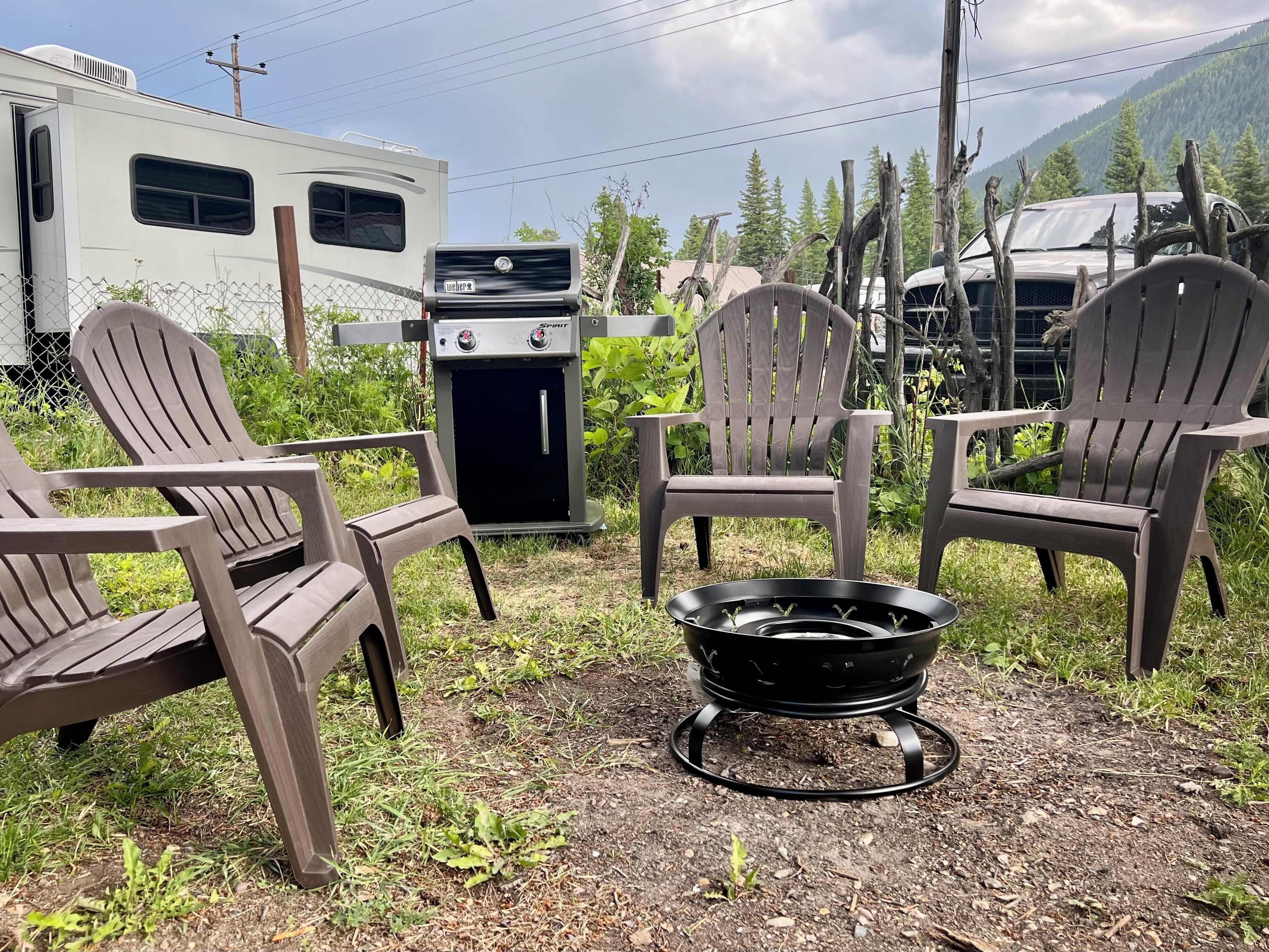 Een buitenzitplaats met Adirondack-stoelen, een draagbare barbecue en een vuurkuil.