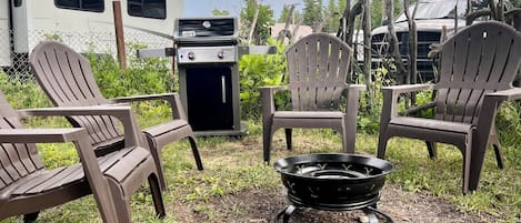 Een buitenzitplaats met Adirondack-stoelen, een draagbare barbecue en een vuurkuil.