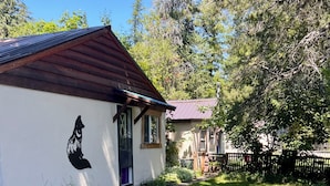 Una cabaña rústica con un mural de lobo, dos sillas Adirondack y una parrilla de metal en un césped.